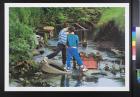 untitled (two boys standing on tires in a garbage-filled body of water)